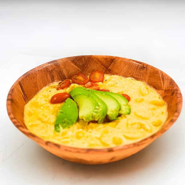 Creamy mac and cheese topped with sliced avocado and cherry tomatoes in a wooden bowl.
