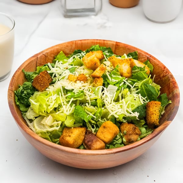 A wooden bowl filled with a fresh Caesar salad, topped with croutons and shredded cheese.