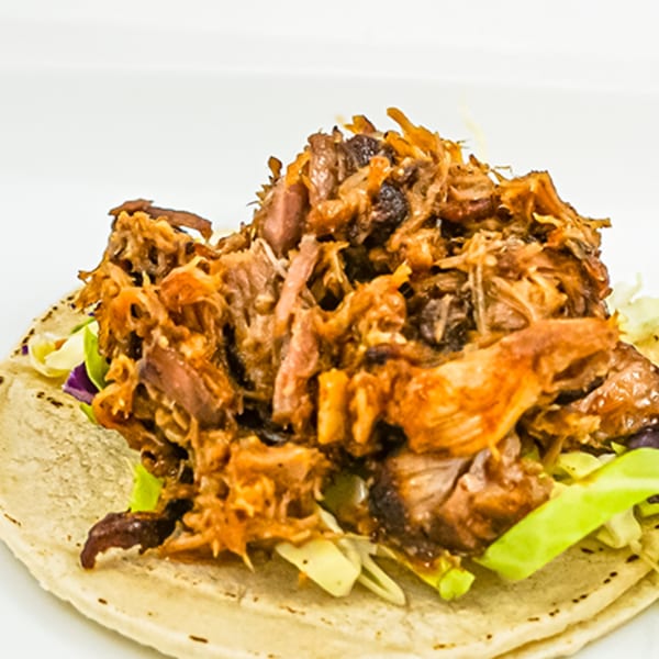 A Ribline BBQ pulled pork taco with green and purple cabbage on a white plate.