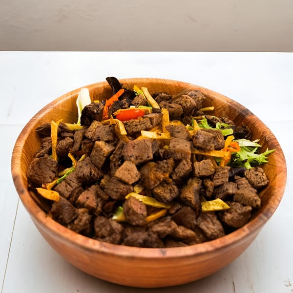 Close-up of a wooden bowl filled with Ribline BBQ's diced brisket, mixed with colorful vegetables.