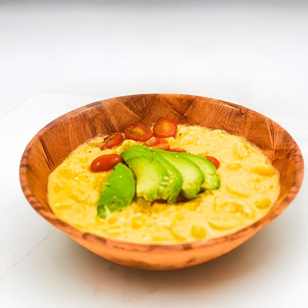 Creamy mac and cheese in a wooden bowl, topped with sliced avocado and cherry tomatoes.