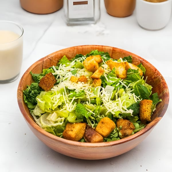A wooden bowl filled with a fresh Caesar salad, topped with croutons and shredded cheese.